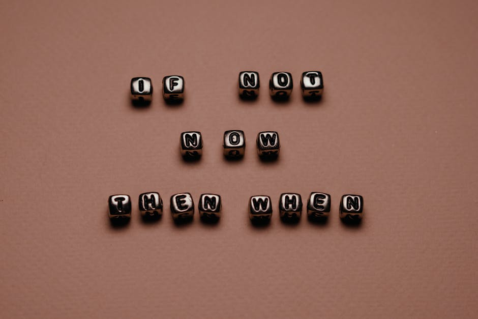 A collection of small black lettered beads arranged on a flat, light brown surface spelling out the phrase 'If not now then when.' The beads are evenly spaced, with the words stacked vertically in three lines, and cast subtle shadows on the surface below. The background is smooth and evenly lit, with no additional objects or environment visible. This image is neutral and straightforward, focusing on the message conveyed through the beads, which can relate to themes of timing and decision-making relevant to house removals or moving services provided by Man with Van Chadwell Heath.
